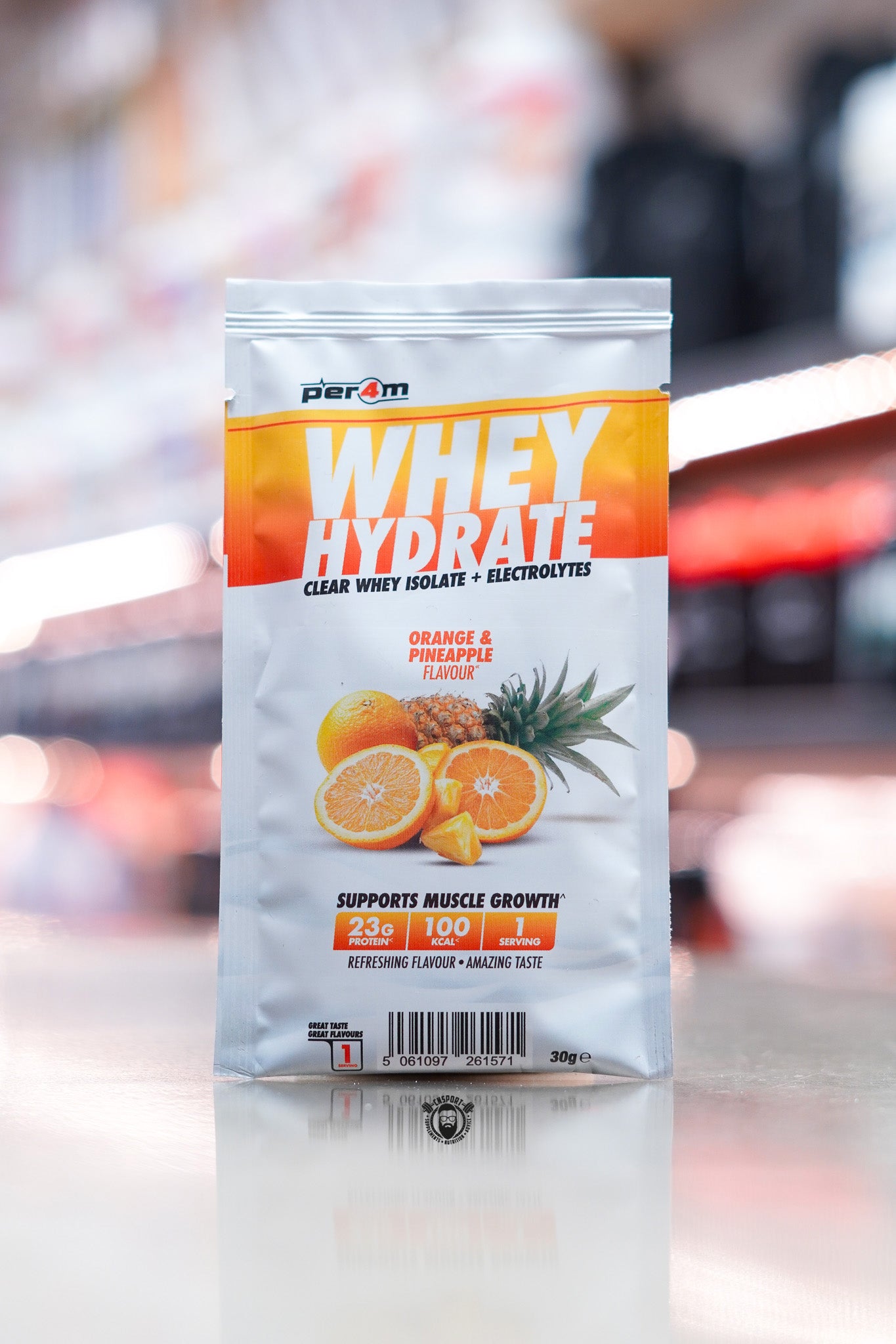 Per4m Whey Hydrate 30g sample sachet, Orange & Pineapple flavour, clear whey isolate with electrolytes, displayed on counter in supplement store.