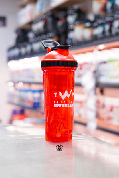 Front view of the TWP Platinum Series 800ml red blender ball shaker with flip-top lid, displayed on a supplement store counter.