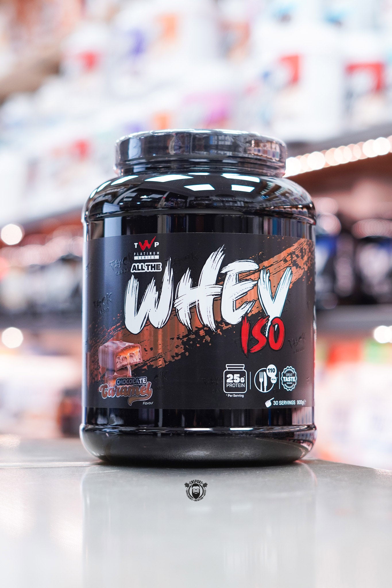 Front-facing image of TWP All The Whey Iso Chocolate Caramel flavour showcasing a rich brown and black label with caramel block visuals.