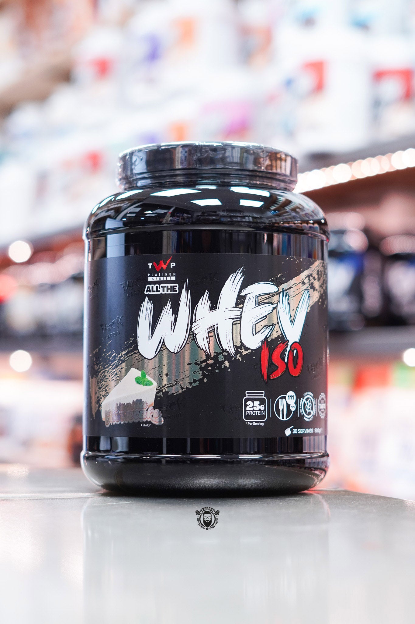 Front-facing image of TWP All The Whey Iso Vanilla Cheesecake flavour featuring a dark design with cheesecake illustration and protein details.