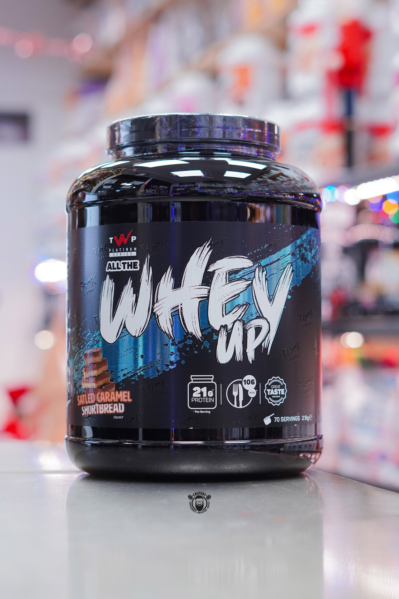 TWP Platinum Series All The Whey Up protein powder in Salted Caramel Shortbread flavour, large black tub displayed on a counter in a supplement store.