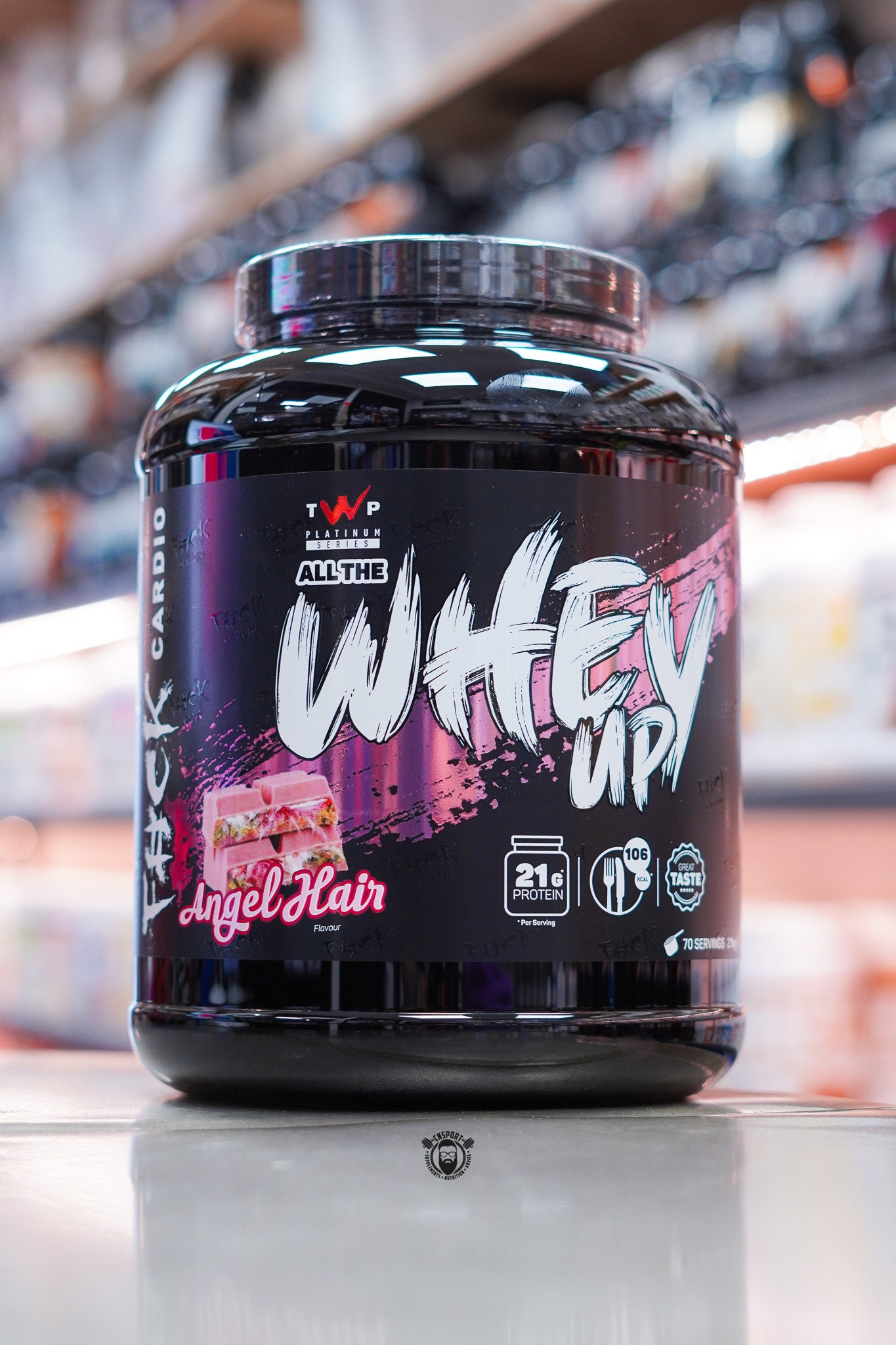 TWP Platinum Series All The Whey Up Angel Hair flavour 2kg whey protein tub on retail counter with blurred supplement store background