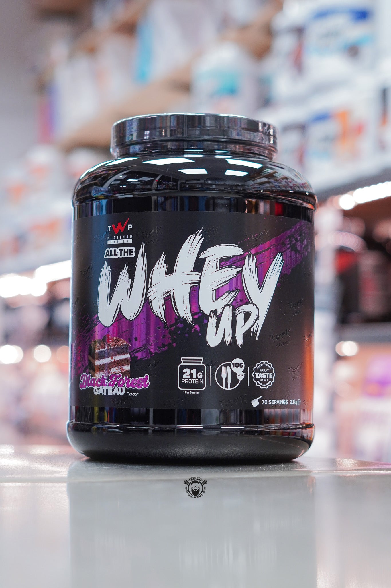 TWP All The Whey Up protein powder, Black Forest Gateau flavour, 2kg tub with 70 servings and 21g protein per serving, displayed on supplement store counter.