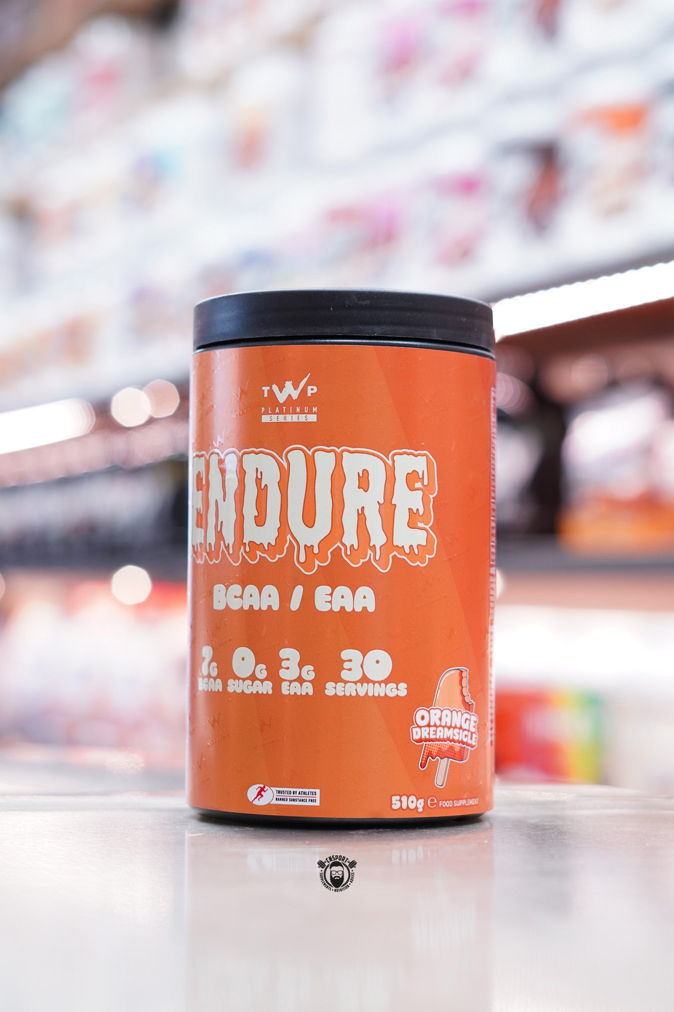 Orange container of TWP Endure BCAA/EAA in Orange Dreamsicle flavour. Label has dripping text and a popsicle graphic, with details showing 7g BCAA, 0g sugar, 3g EAA, and 30 servings.