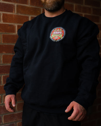 Man wearing a black WRPF UK sweatshirt with the federation’s crest logo on the left chest, standing against a brick wall background.